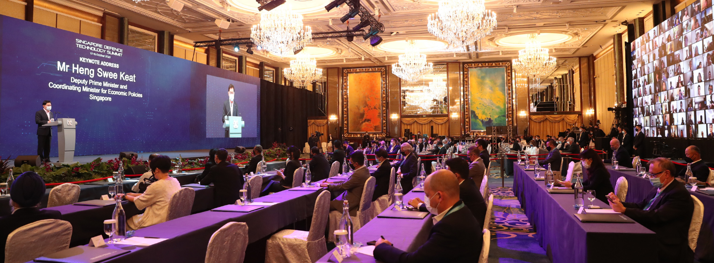 Mr. Heng Swee Keat speaks onstage at Singapore Defence Tech Summit, attendees with masks, video wall background.